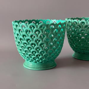 May include: Two teal-colored bowls featuring an intricate, openwork lattice pattern composed of repeating arched, scale-like shapes. Each bowl has a wide, circular base and a scalloped rim, creating a textured, decorative appearance.