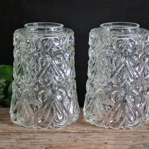 Könnte beinhalten: Zwei klare Glasschirme mit einem dekorativen, geprägten Muster. Das Muster ist ein sich wiederholendes Design aus Wirbeln und Schleifen.