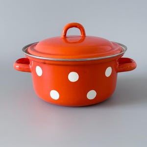 Puede incluir: Una olla de cocina de esmalte naranja brillante con tapa, asas laterales y lunares blancos. La olla tiene un borde plateado y un asa de bucle en la tapa. Un utensilio de cocina clásico.