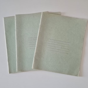 Peut inclure: Trois cahiers en papier vert avec des pages lignées. Les cahiers sont empilés les uns sur les autres.