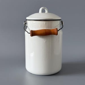 Peut inclure: Une cruche à lait en émail blanc avec un couvercle et une poignée en bois. La cruche a un bord noir et une poignée en fil de fer. La poignée en bois est de couleur marron chaud. Design classique et vintage.