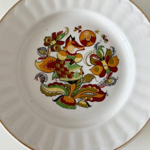 Pode incluir: Prato de cerâmica branco com borda dourada e um design de arte popular colorido com uma raposa, flores e folhas. O design é em tons de vermelho, laranja, amarelo, verde e marrom.