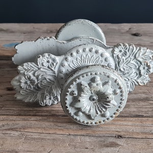 Puede incluir: Un juego de tres pomos de puerta de metal blanco adornados con diseños florales. Los pomos son de estilo vintage y tienen un acabado desgastado.