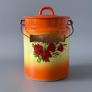 May include: An orange and yellow enamelware container with a lid and a wooden handle. The container features a floral design of red poppies. A metal wire handle is attached to the sides.