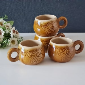 May include: Set of four brown ceramic coffee mugs with a swirling pattern. The mugs have a light brown interior and a darker brown exterior.