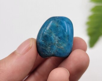 May include: A smooth, polished blue apatite tumbled stone. The stone has a light blue color with darker blue streaks and swirls.