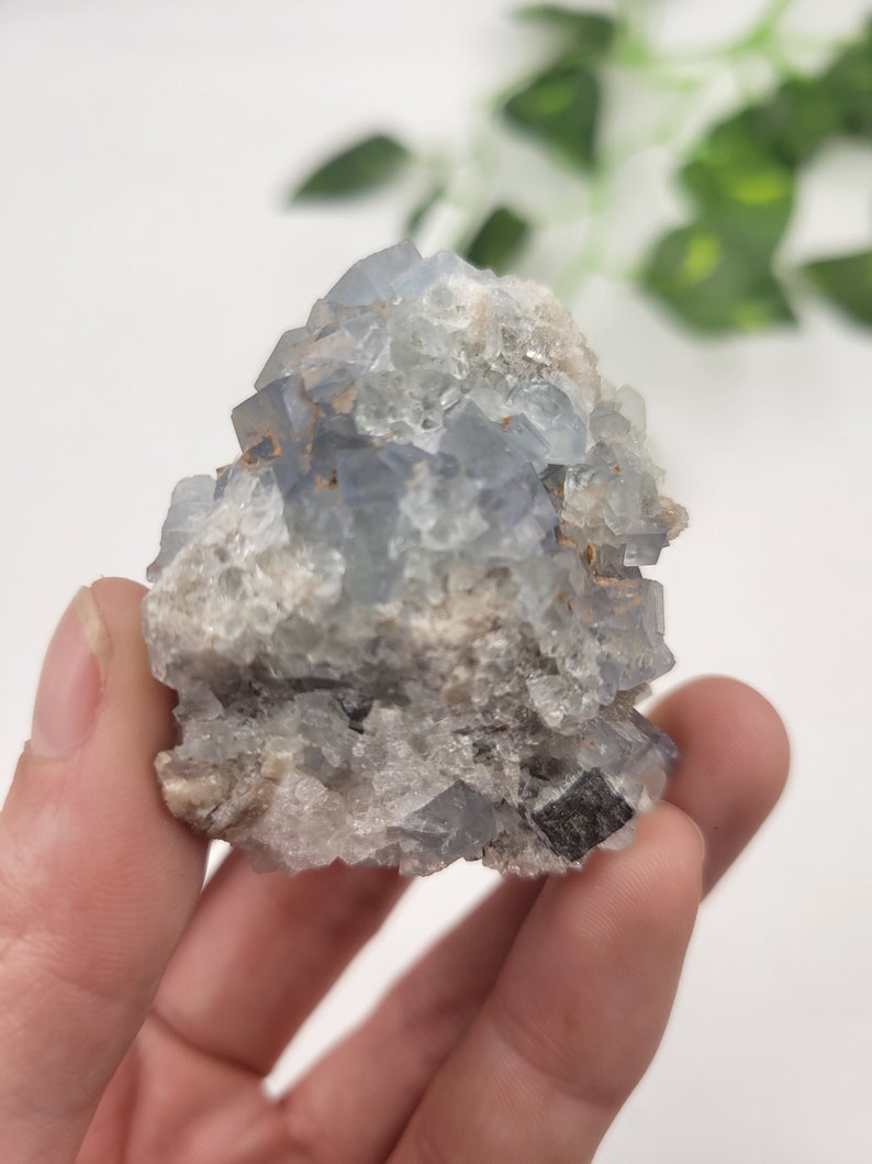 May include: A cluster of blue fluorite crystals with a rough, natural texture. The crystals are a light blue color and have a slightly iridescent sheen.