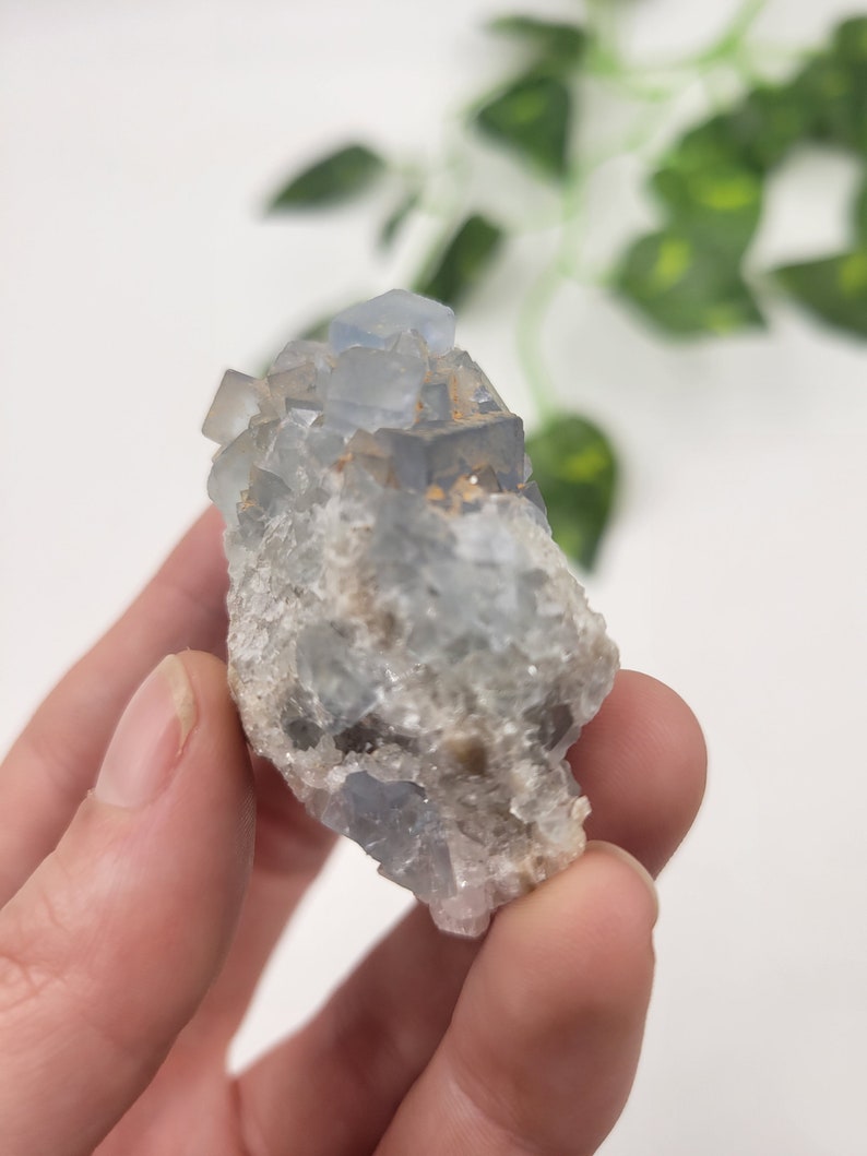 May include: A cluster of light blue fluorite crystals with a rough, natural texture. The crystals are clustered together in a small, irregular shape.