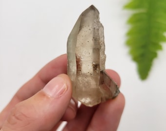 May include: A clear quartz crystal with a smoky brown hue. The crystal is double terminated and has a natural, raw appearance.