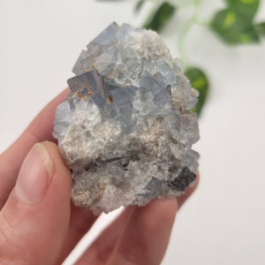 May include: A cluster of blue fluorite crystals with a rough, natural texture. The crystals are clustered together in a pyramid shape, with some smaller crystals surrounding the larger ones.
