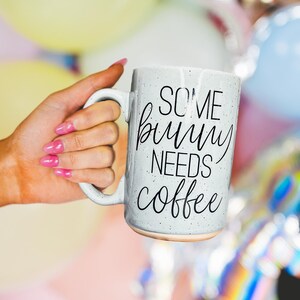 Könnte beinhalten: Eine weiße Keramik-Kaffeetasse mit schwarzem Text, der "Some bunny needs coffee" lautet.