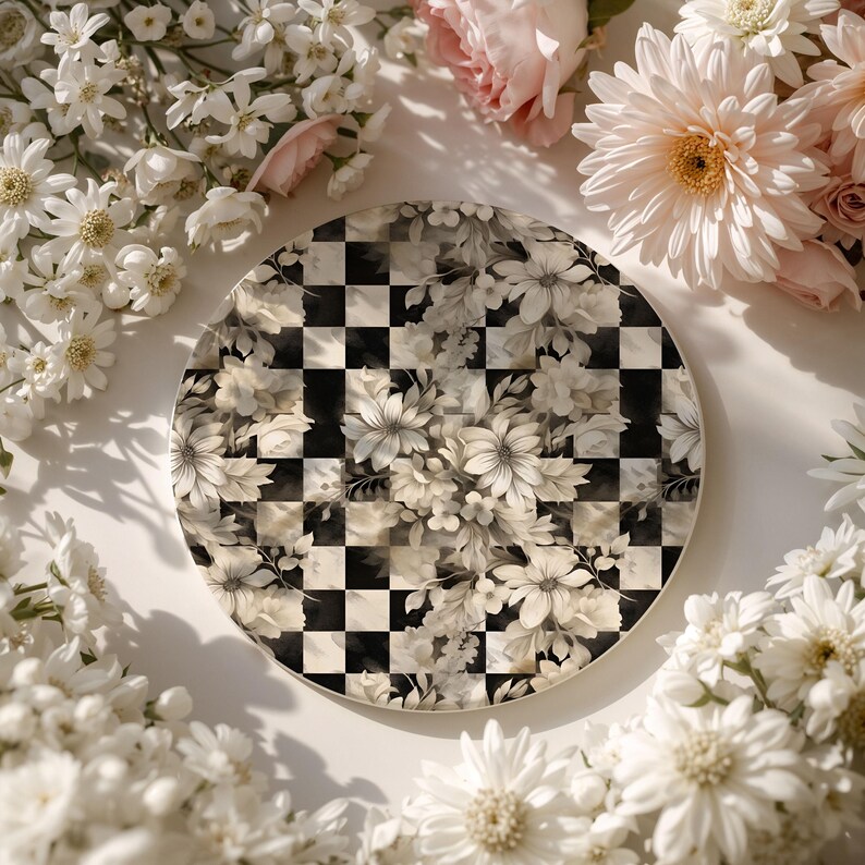 Op de afbeelding: Een ronde decoratieve plaat met een zwart-wit geblokt patroon, bedekt met een bloemenontwerp in wit- en cr&egrave;metinten. De plaat is omgeven door witte en roze bloemen.
