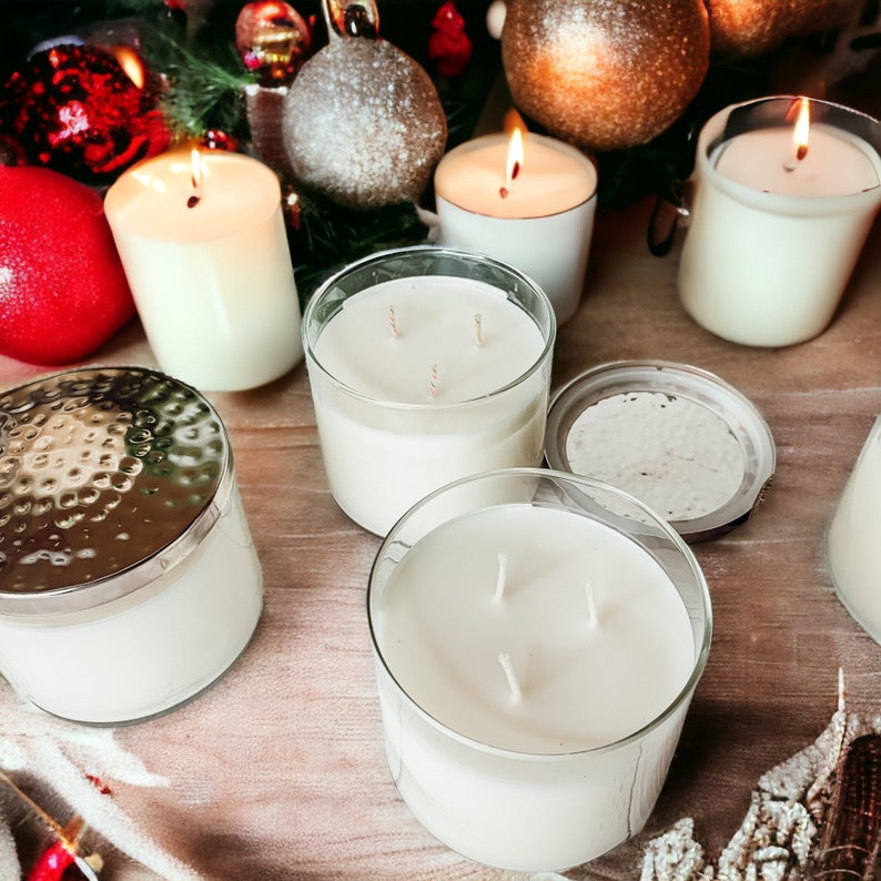 May include: A collection of six white candles in various glass containers. Some candles have multiple wicks. The candles are arranged on a wooden surface with holiday decorations.