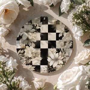Op de afbeelding: Een ronde decoratieve plaat met een zwart-wit geblokt patroon en bloemaccenten. De plaat is omgeven door witte rozen en andere bloemen, wat een romantische en elegante uitstraling cre&euml;ert.