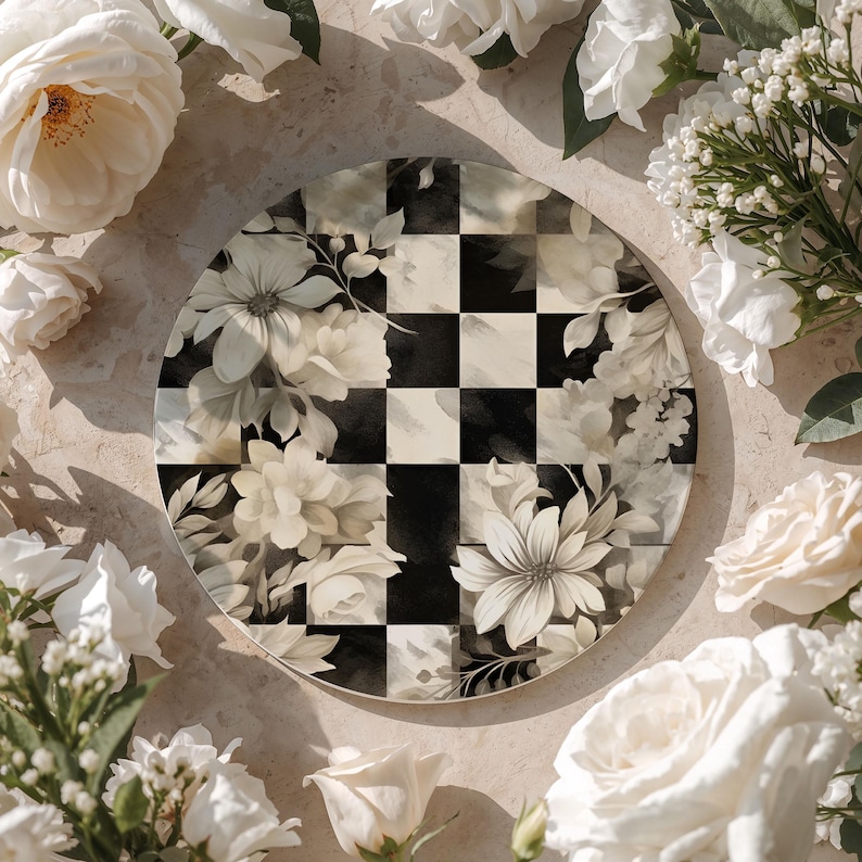 Op de afbeelding: Een ronde decoratieve plaat met een zwart-wit geblokt patroon en bloemaccenten. De plaat is omgeven door witte rozen en andere bloemen, wat een romantische en elegante uitstraling cre&euml;ert.