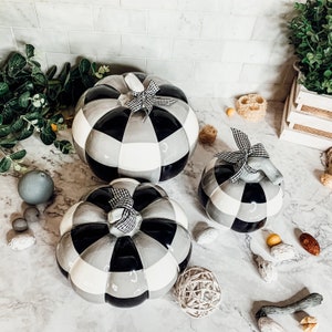 May include: Three ceramic pumpkins in a black and white checkered pattern. The pumpkins are different sizes and are arranged on a white surface.