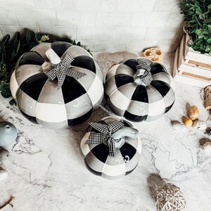 May include: Three black and white ceramic pumpkins with a checkered pattern. The pumpkins are decorated with black and white ribbon bows.