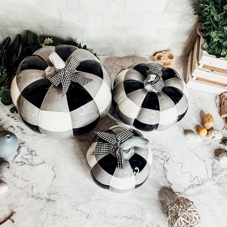 May include: Three black and white ceramic pumpkins with a checkered pattern. The pumpkins are decorated with black and white ribbon bows.