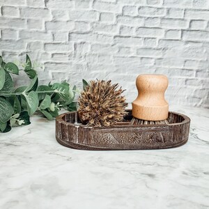 May include: A wooden dish with two brown dish brushes. One brush has a wooden handle and the other has a natural bristle head.
