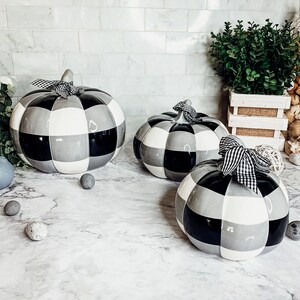 May include: Three ceramic pumpkins in a black and white checkered pattern. The pumpkins are different sizes and have black ribbon bows.