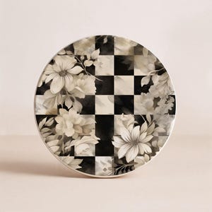 Op de afbeelding: Ronde decoratieve plaat met een zwart-wit geblokt patroon en bloemenontwerp. De bloemen zijn in tinten wit en grijs, wat een vintage esthetiek cre&euml;ert. De plaat heeft een witte rand.