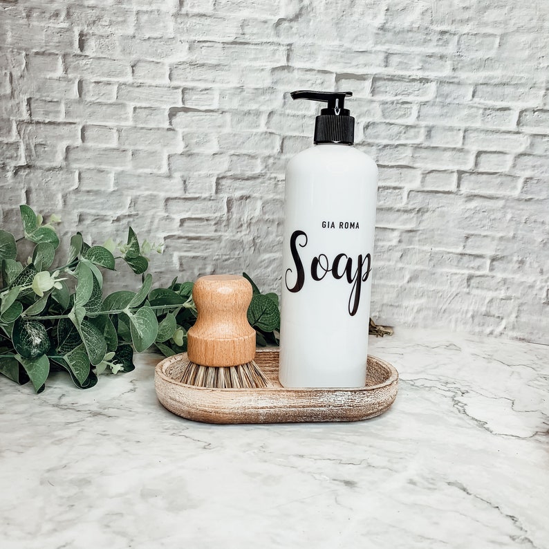 May include: White ceramic soap dispenser with a black pump and the text "Gia Roma Soap" on the front. The dispenser is sitting on a wooden tray with a wooden brush.