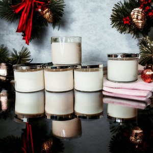May include: Six unscented candles in clear glass jars with silver lids. The candles are arranged in a pyramid shape on a black surface. The candles are surrounded by a pink towel and a few decorative items.