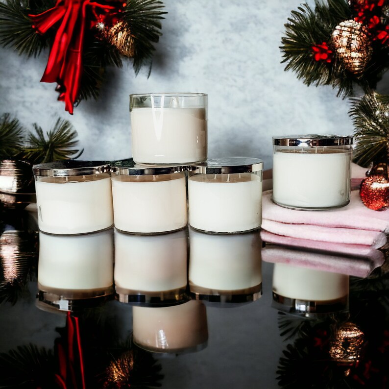 May include: Six unscented candles in clear glass jars with silver lids. The candles are arranged in a pyramid shape on a black surface. The candles are surrounded by a pink towel and a few decorative items.