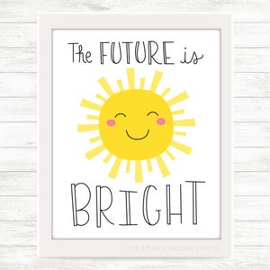May include: A white framed print with a yellow sun with a smiling face and the text "The FUTURE is BRIGHT" in black.