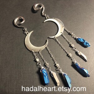 May include: Silver-toned crescent moon earrings with dangling chains, stars, and blue crystal accents. The earrings have a spiral design at the top and are displayed on a dark surface. The Etsy shop name "hadalheart.etsy.com" is visible.