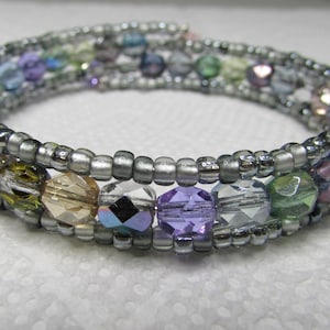May include: A silver wire wrapped bracelet with multi-colored glass beads. The beads are in shades of purple, green, blue, and brown.