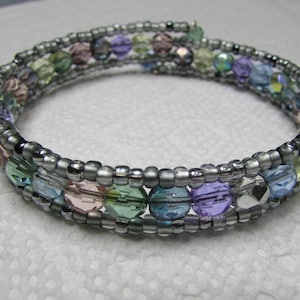 May include: A silver wire wrapped bracelet with multi-colored glass beads. The beads are in shades of blue, green, purple, and pink.