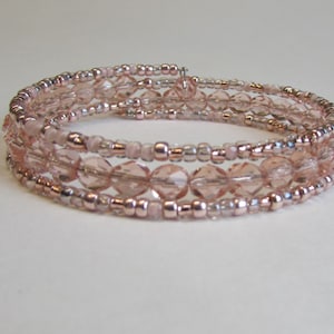 May include: A triple-strand rose gold beaded bracelet with clear and pink beads. The bracelet is made with small seed beads and larger faceted beads.