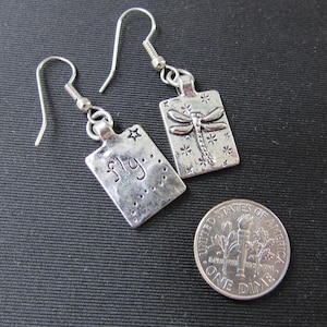 May include: Silver dangle earrings with a dragonfly charm on one earring and the word "fly" on the other earring.