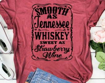 Può includere: Una maglietta color marsala con una grafica nera che recita "Smooth as Tennessee Whiskey Sweet as Strawberry Wine".