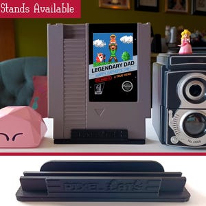 May include: Three different types of stands for video game cartridges. The stands are made of black plastic and have a simple design. The stands are labeled "Pixel Art &" and "No. 0668".