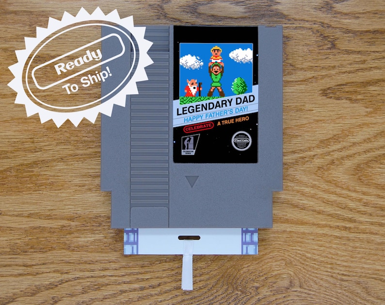 A Father’s Day greeting card is made from a reproduction NES cart. It has a glossy label and a flat card that goes inside the game cart with a ribbon attached. Label art Link holding up a child with an old man next to him.