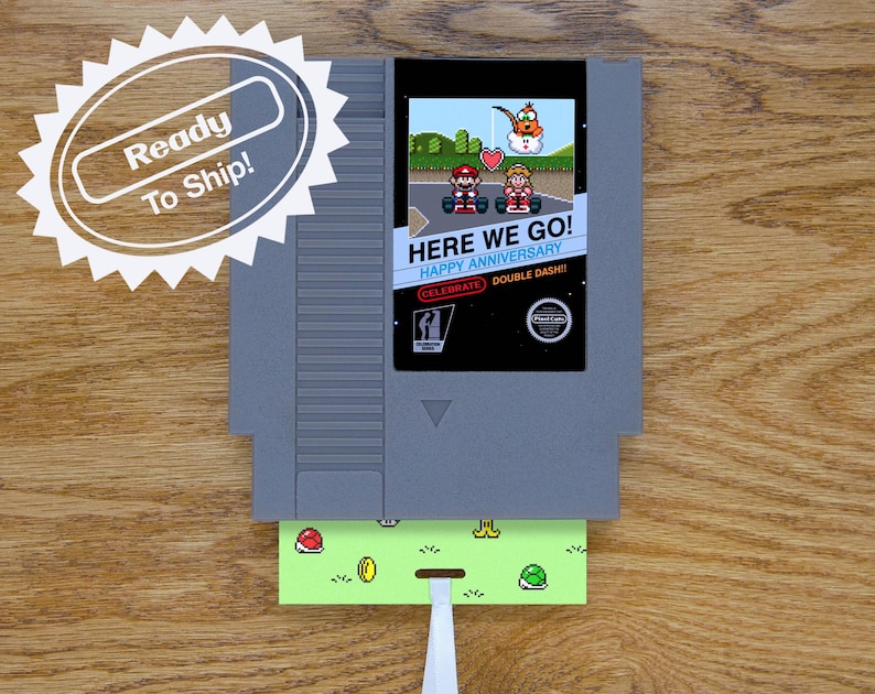 A greeting card is made from a reproduction NES cart. It has a glossy label and a flat card that goes inside the game cart with a ribbon attached. On the label, Mario and Peach are ready to race with a heart overhead in a scene from Mario Kart.