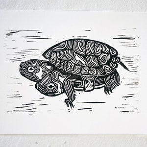May include: Black and white linocut print of a turtle with its head and legs extended. The turtle is depicted in a stylised, abstract manner, with intricate lines and patterns.