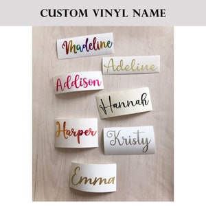 May include: Seven custom vinyl name decals featuring various script fonts and colours, including rainbow gradient, gold, hot pink, black, and silver. The names displayed are Madeline, Adeline, Addison, Hannah, Harper, Kristy, and Emma on white backing.