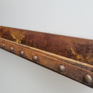May include: Rustic wooden shelf with a metal trim and decorative metal studs. The shelf has a distressed, rusty finish.