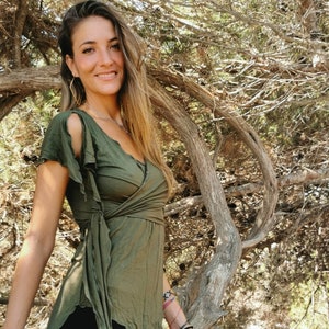 Può includere: Un top avvolgente verde oliva con maniche corte e un design fluido. Il top è abbinato a pantaloncini neri. L'outfit ha un'estetica naturale e bohémien. Il top presenta un design avvolgente unico.