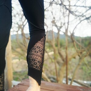 May include: Black leggings with a lace panel on the lower leg. The leggings are worn by a person standing on a wooden deck.