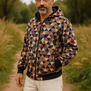 Puede incluir: Chaqueta con capucha y cremallera con un patrón geométrico de triángulos en tonos marrón, naranja, azul y verde. La chaqueta tiene puños negros, forro de capucha negro y ribetes negros. La persona lleva pantalones beiges.
