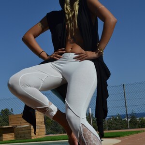 May include: A woman wearing a black hooded top with white pants and lace trim. She is standing by a pool with a fence in the background.