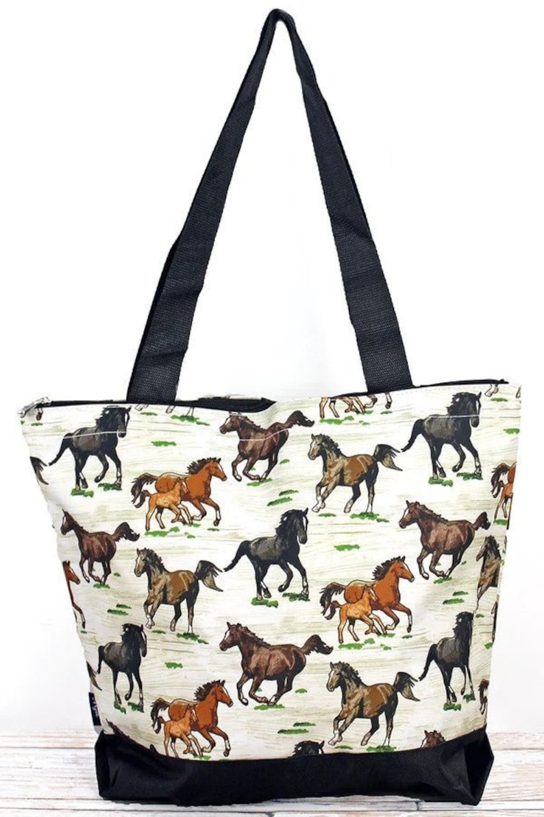May include: A white tote bag with a black zipper and black handles. The bag features a pattern of brown and black horses running on a white background.