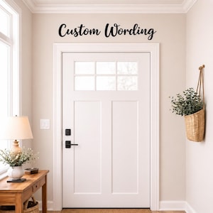 May include: A white door with a black handle and the words "Custom Wording" above it. A small wooden table with a lamp and flowers sits to the left of the door. A hanging basket with greenery is on the right.