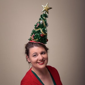 May include: A woman wearing a red sweater and a green Christmas tree hat with a gold star on top. The text "Jezebel's Fascination" is written in pink letters at the bottom of the image.