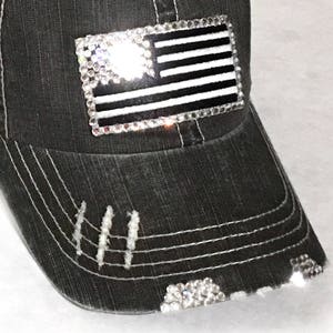 May include: A black denim baseball cap with a distressed look. The cap features a rhinestone American flag design on the front.