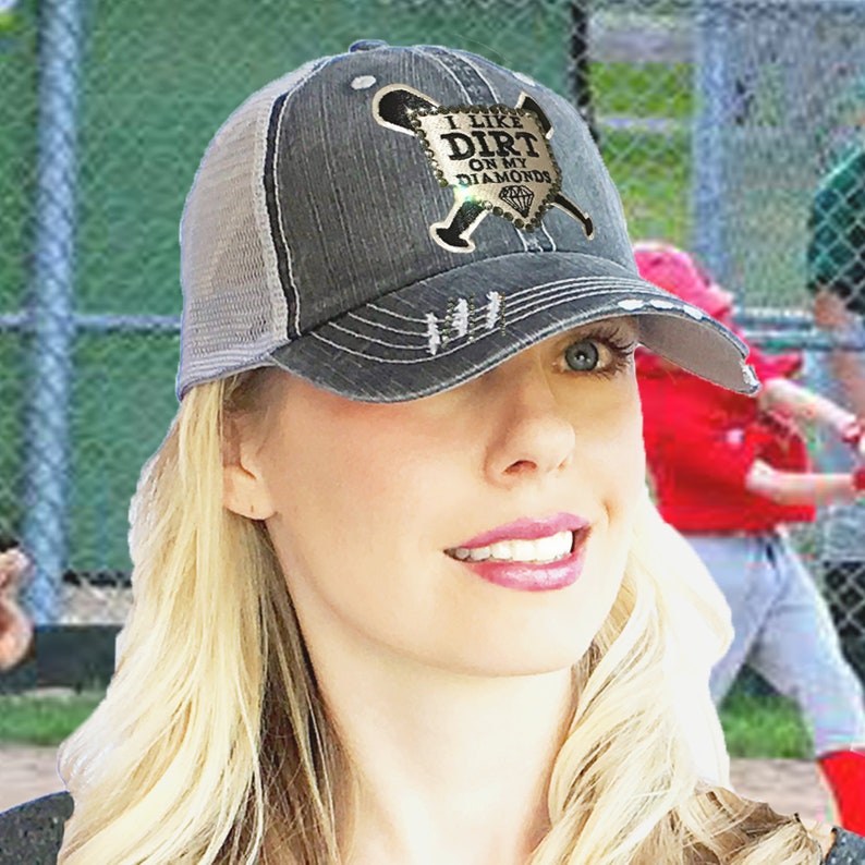 May include: A black and gray distressed baseball cap with a mesh back. The cap has a gold-colored patch with the text "I like dirt on my diamonds" and a baseball bat and ball graphic.